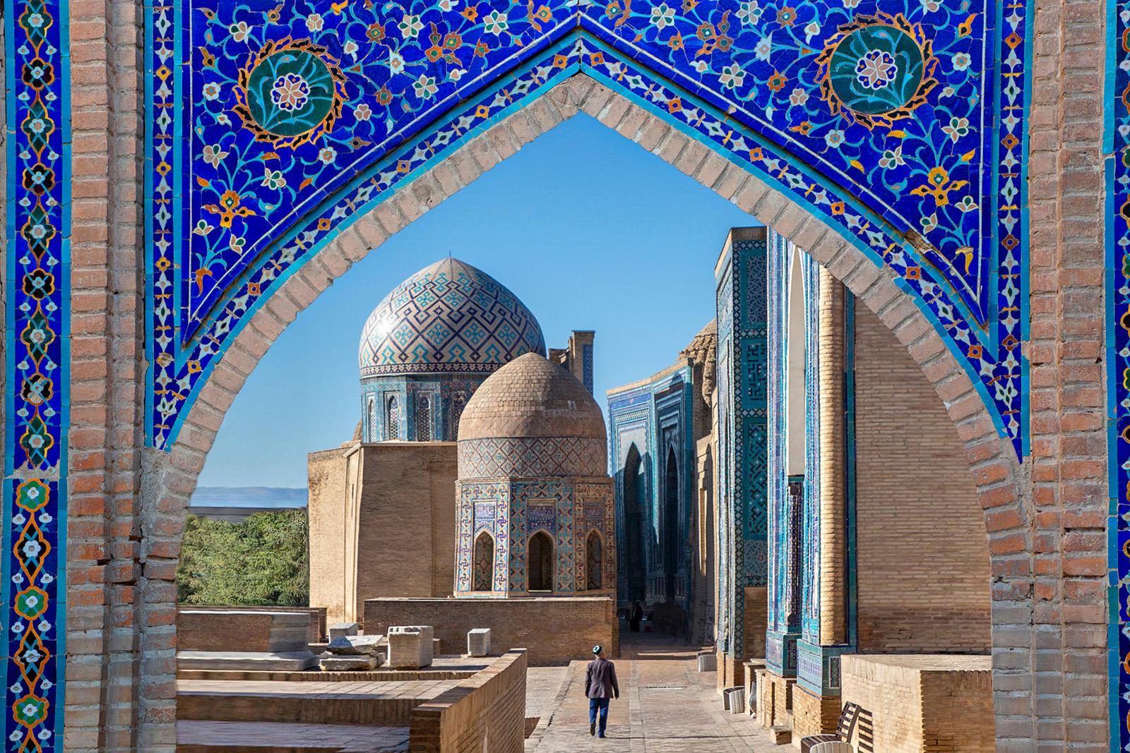 View over the mausoleums and domes of the historical cemetery of Shahi Zinda through an arched gate,
